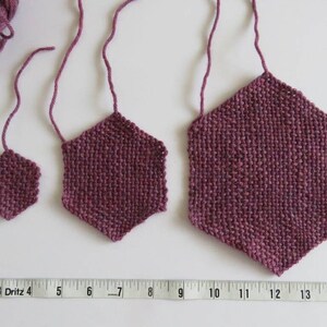 May include: Three crocheted hexagons in different sizes, all in a deep burgundy colour. The hexagons are hanging from a white surface.