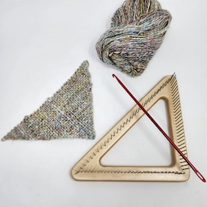 May include: A craft image showing a wooden triangular knitting loom with metal pegs, a red crochet hook, a small knitted triangle, and a ball of multicoloured yarn. The yarn is in shades of brown, green, and blue.