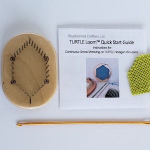 May include: A wooden hexagon-shaped loom with a set of metal pins. The loom is used for weaving with yarn. A green woven piece is shown in the background. The text on the card reads "TURTLE Loom&trade; Quick Start Guide Instructions for Continuous Strand Weaving on TURTLE Hexagon Pin Looms".