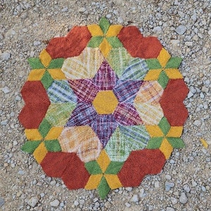 May include: A colorful, geometric rug with a starburst pattern in shades of red, yellow, green, and white. The rug is made of woven fabric and has a textured surface.