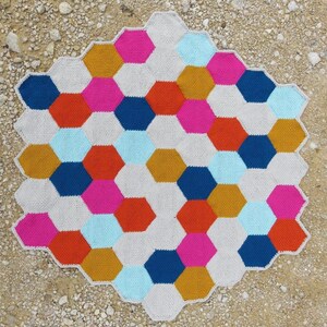 May include: A crocheted hexagon blanket with a geometric pattern in shades of pink, red, orange, yellow, blue, and white.