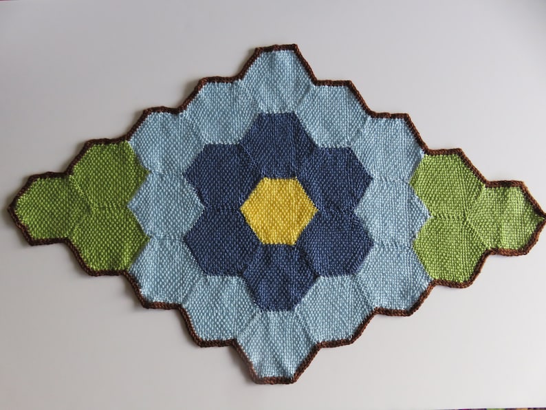 May include: A knitted throw rug with a geometric pattern in shades of blue, green, and yellow. The rug is edged in brown yarn.