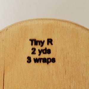 May include: Close-up of a wooden spool with the text "Tiny R 2 yds 3 wraps" printed on it.