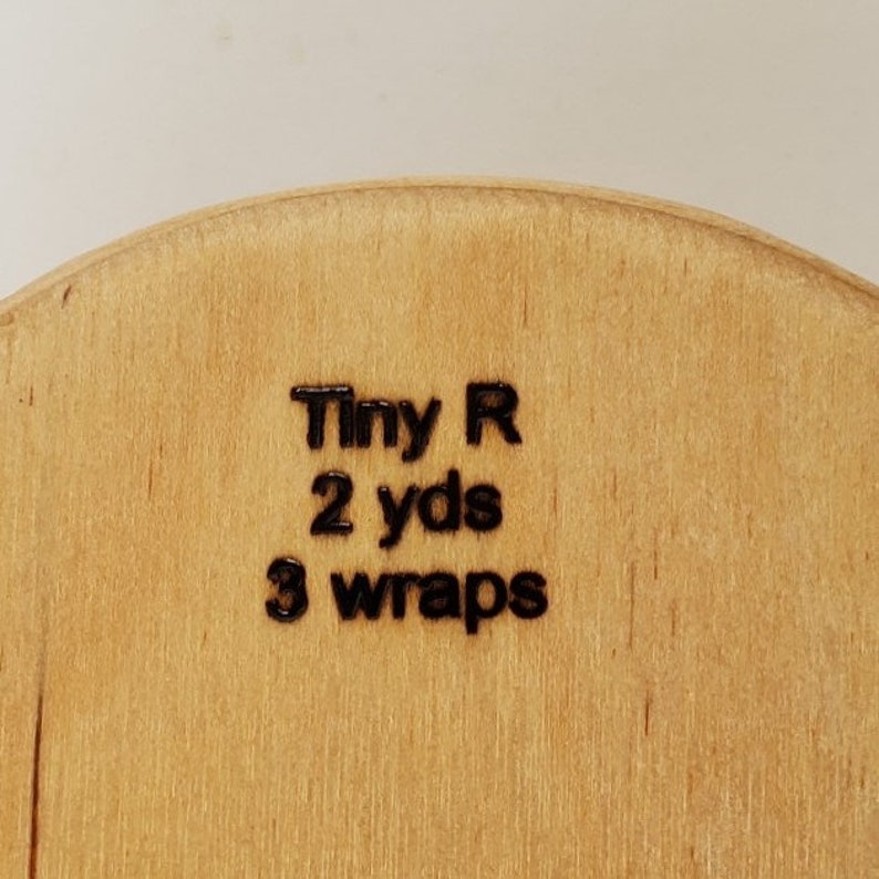 May include: Close-up of a wooden spool with the text "Tiny R 2 yds 3 wraps" printed on it.