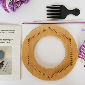May include: A wooden round loom with a hexagonal pin loom, purple and white yarn, a purple crochet hook, a black comb, and instructions for continuous strand weaving on TURTLE Hexagon Pin Looms.