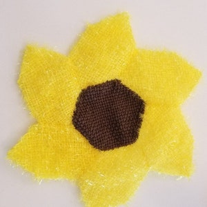 May include: A yellow sunflower-shaped bath sponge with a brown centre. The sponge is made of a soft, fluffy material.