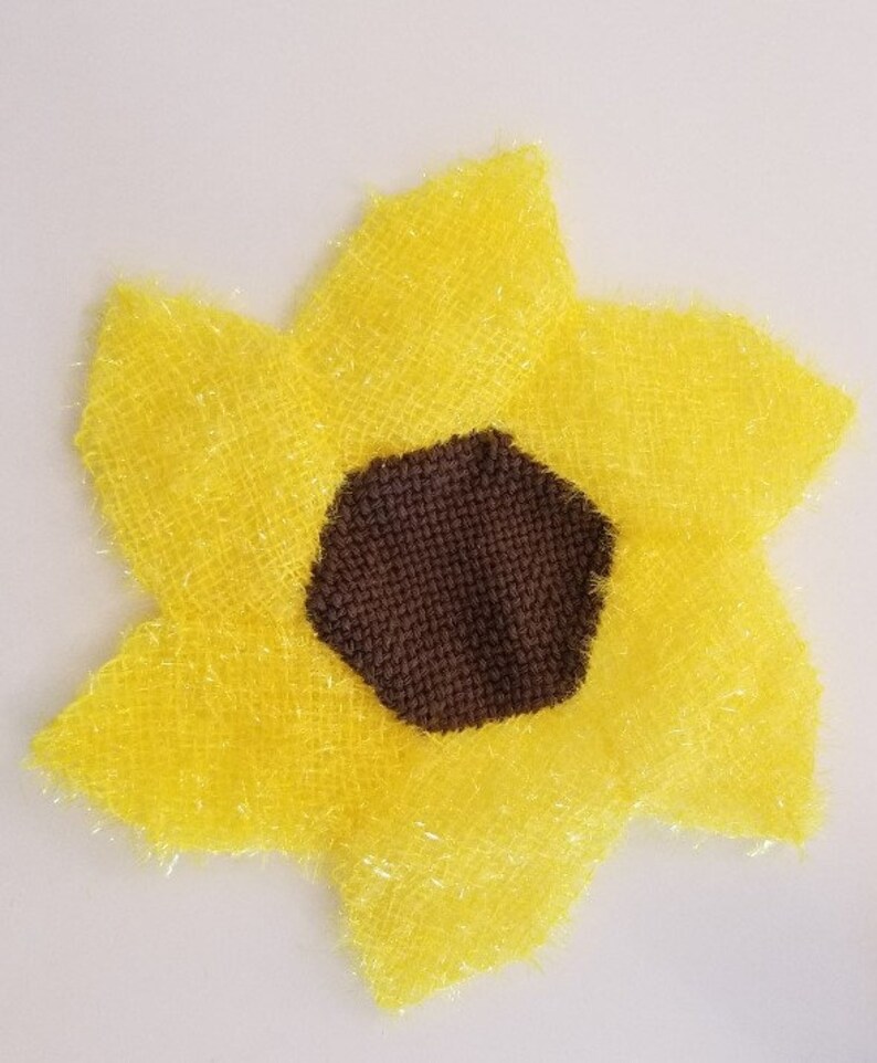 May include: A yellow sunflower-shaped bath sponge with a brown centre. The sponge is made of a soft, fluffy material.