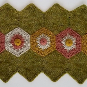 May include: A green crocheted table runner with a scalloped edge and five crocheted flower designs in shades of pink, white, and yellow.