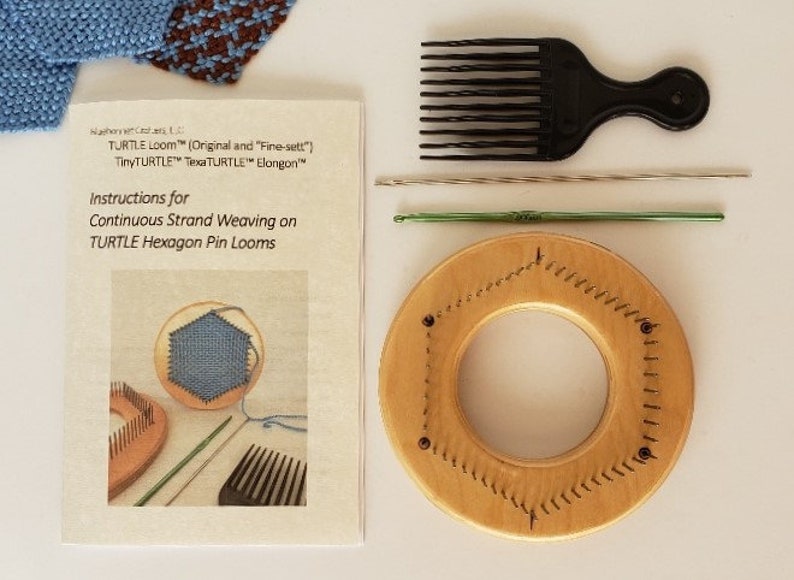 May include: A wooden hexagon pin loom with instructions for continuous strand weaving. The loom is light brown and has a hole in the center. The instructions are printed on a white sheet of paper and include the text "TURTLE Loom&trade; (Original and "Fine-sett") TinyTURTLE&trade; Texa TURTLE&trade; Elongon" and "Instructions for Continuous Strand Weaving on TURTLE Hexagon Pin Looms".