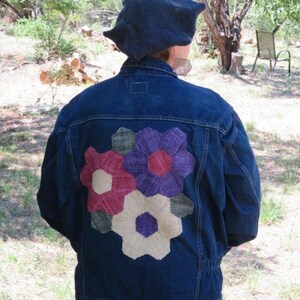 May include: A blue denim jacket with a colourful flower patch on the back. The patch is made of fabric and has a variety of colours, including red, purple, green, and white.