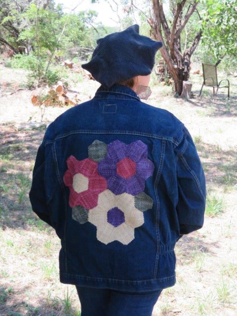 May include: A blue denim jacket with a colourful flower patch on the back. The patch is made of fabric and has a variety of colours, including red, purple, green, and white.