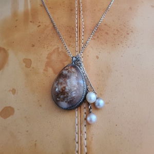 May include: A silver chain necklace with a brown and white shell pendant and three white pearl charms.