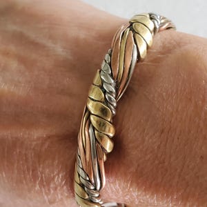 May include: A mixed-metal bracelet featuring a woven design. The bracelet incorporates gold, silver, and copper tones, creating a textured and eye-catching accessory. The bracelet is approximately 2 inches in diameter.