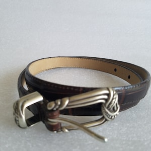 May include: A brown leather belt with a silver buckle. The buckle has a decorative design.