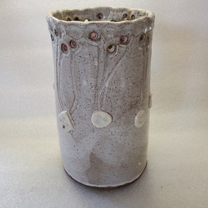 May include: A white ceramic vase with a textured surface and a floral design. The vase has a scalloped rim and is decorated with small, raised dots and circles.