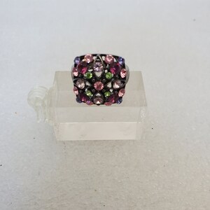 May include: A silver ring with a square-shaped design featuring a cluster of pink, purple, and green rhinestones.