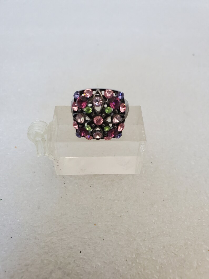 May include: A silver ring with a square-shaped design featuring a cluster of pink, purple, and green rhinestones.
