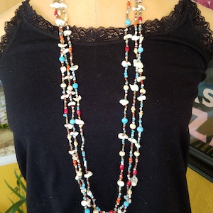 May include: A multi-strand necklace made of white, turquoise, red, and gold beads. The necklace is layered and features a variety of shapes and sizes of beads.