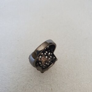 May include: A black ring with a square-shaped design and pink stones.