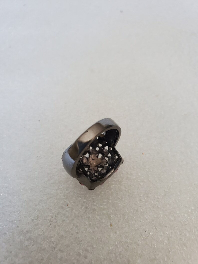 May include: A black ring with a square-shaped design and pink stones.