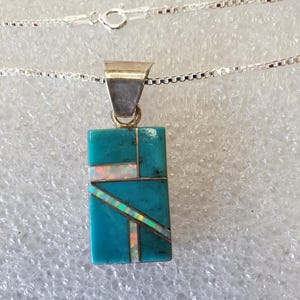 May include: A turquoise and white pendant necklace with a geometric design. The pendant is made of turquoise and opal stones and is set in sterling silver.