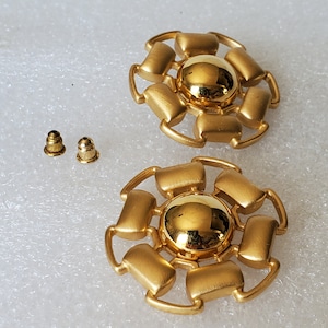 May include: A pair of gold tone earrings with a circular design. Each earring features a central round gold tone piece surrounded by eight smaller rectangular pieces.