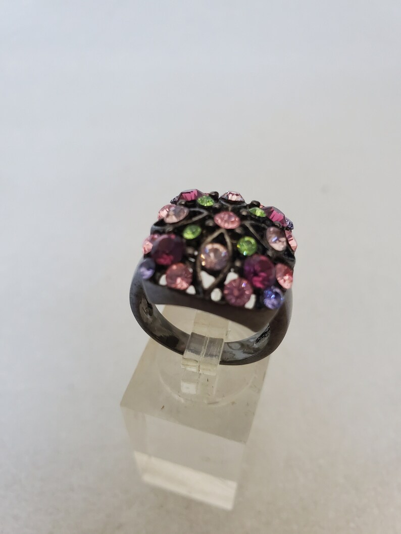 May include: A black ring with a square-shaped setting adorned with colorful rhinestones in shades of pink, green, and purple.