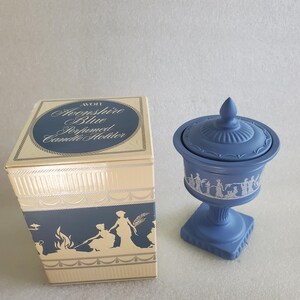 May include: A blue Avon 'Avonshire Blue Perfumed Candle Holder' with a matching box. The box and candle holder feature white classical figures and decorative trim. The candle holder is a lidded urn on a pedestal base.