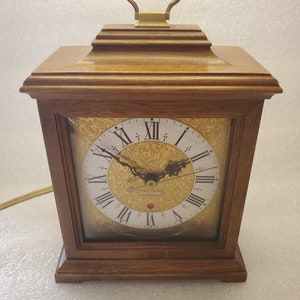 May include: A wooden clock with a gold face and black Roman numeral markings. The clock has a brass handle on top and says "Seth Thomas" on the face.