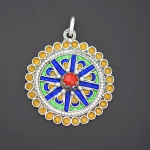 May include: A silver pendant with a round, colorful design. The pendant features a central red stone surrounded by blue, green, and yellow enamel. The pendant is decorated with a silver border of small beads.