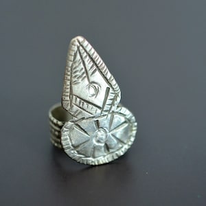 Può includere: Un anello d'argento con un design geometrico. L'anello ha una fascia larga e una parte superiore grande e decorata.