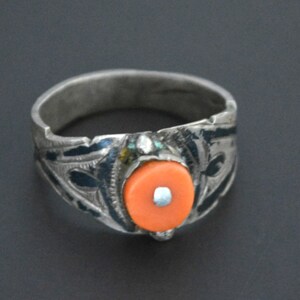 May include: A silver ring featuring an elaborate design and a bright orange stone set in the centre.