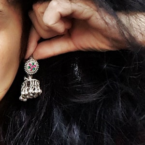 May include: A silver dangle earring with a round, multi-coloured stone and a teardrop-shaped pendant with silver beads.