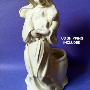 May include: White ceramic figurine of a woman holding a child. The figurine is a planter with a pot on the bottom.