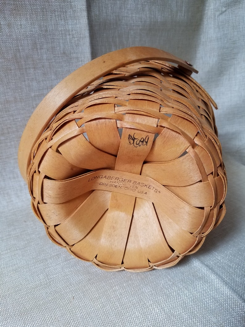 Puede incluir: Una cesta tejida de color marr&oacute;n con asa. La cesta est&aacute; etiquetada con "Longaberger Baskets" y "Handwoven" con la ubicaci&oacute;n "Dresden, Ohio USA". El n&uacute;mero "509" est&aacute; escrito en la parte inferior de la cesta.