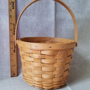Puede incluir: Una peque&ntilde;a cesta tejida natural con un solo asa. La cesta est&aacute; hecha de madera marr&oacute;n claro y tiene un patr&oacute;n tejido. La cesta mide aproximadamente 15 cm de alto.