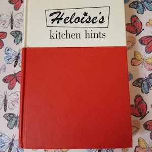 May include: A red hardback book with the title "Heloise's kitchen hints" printed in black on a white background. The book has a white spine and a red back cover.