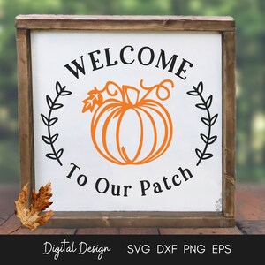 May include: A white wooden sign with a black and orange pumpkin design. The sign reads "Welcome to Our Patch" with a wreath of leaves around the pumpkin.