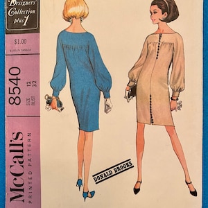 Op de afbeelding: Een vintage McCall's naaipatroon voor een jurk, maat 12, borstomvang 32. Het patroon is voor een eenvoudige, elegante jurk met lange mouwen en een knoopsluiting aan de voorkant. Het patroon is uit de New York Designers Collection, plus 1. Het patroon is geïllustreerd met twee vrouwen die de jurk in verschillende kleuren dragen.