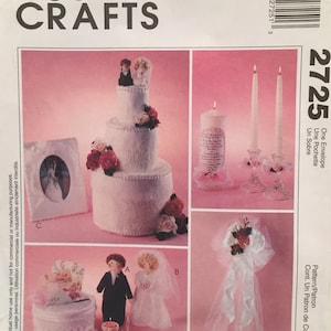 Könnte beinhalten: Ein Bastelmuster zum Thema Hochzeit mit einer dreistöckigen Torte, einer Braut- und Bräutigam-Puppe, einer Kerze, einem Bilderrahmen und einer Schleife. Das Muster trägt den Titel "2725 One Envelope Un Sobre" und stammt von McCall's Crafts.