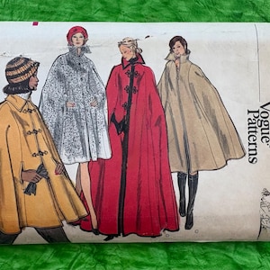 May include: Vintage Vogue Patterns envelope with illustrations of capes. The envelope shows a mustard yellow cape, a patterned cape, a red cape with black trim, and a tan cape. The text on the envelope reads "Very Easy Vogue Patterns" and "Misses' Medium 12-14".