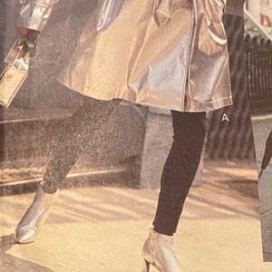 Puede incluir: Una gabardina plateada met&aacute;lica con cintur&oacute;n y cierre de doble botonadura. La modelo lleva pantalones negros y zapatos plateados. La imagen tiene el texto "VOGUE SPORT" en la parte inferior.