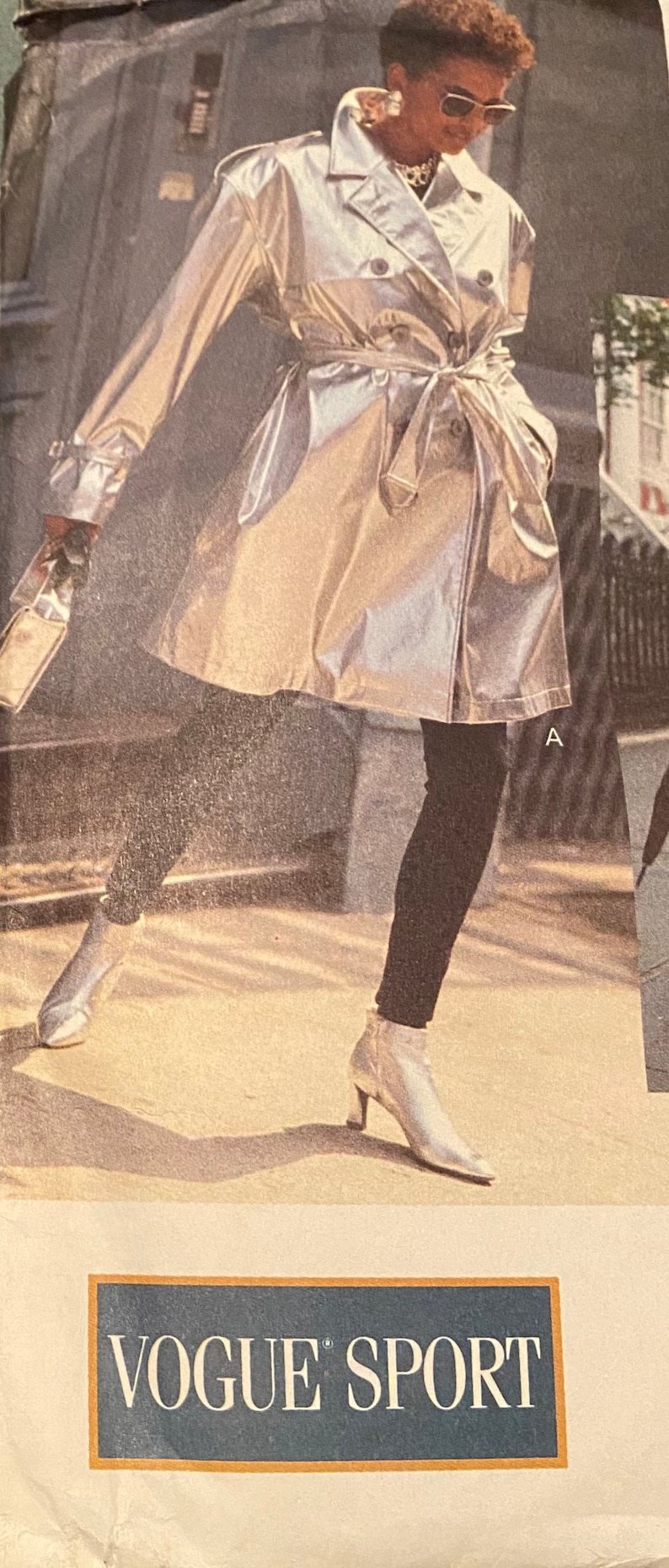 Puede incluir: Una gabardina plateada met&aacute;lica con cintur&oacute;n y cierre de doble botonadura. La modelo lleva pantalones negros y zapatos plateados. La imagen tiene el texto "VOGUE SPORT" en la parte inferior.