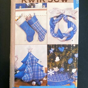 Op de afbeelding: Kwik Sew kerstdecoratiepatroon. De afbeelding toont een verscheidenheid aan kerstversieringen, waaronder kousen, een krans, een boom en ornamenten. De decoraties zijn voorzien van blauw-wit geruite stof en sneeuwvlokborduurwerk.