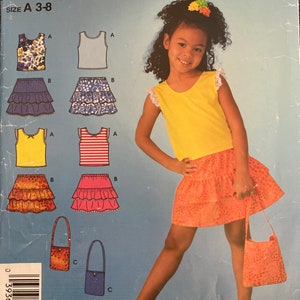 May include: Simplicity sewing pattern for girls' outfits, featuring tops, tiered skirts, and a handbag. The pattern includes floral and striped tops, and skirts in various colours. The girl in the image is wearing a yellow top and orange skirt.