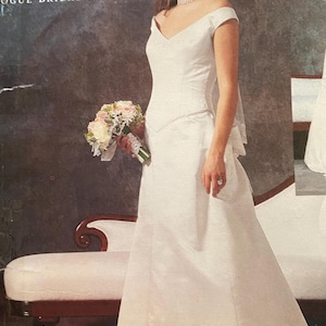 May include: A white wedding dress with a V-neck and off-the-shoulder sleeves. The dress is paired with a bouquet of flowers. The text "BELLVILLE SASSOON" and "VOGUE BRIDAL ORIGINAL" are visible in the image.