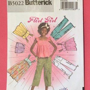 May include: A sewing pattern for a girl's outfit. The pattern includes a pink top, a green pair of pants, and a few different skirt options. The pattern is called "Flirt Girl" and is from Butterick, pattern number B5022.