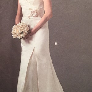 May include: A strapless ivory wedding dress with a sweetheart neckline and a floral accent at the waist. The dress features a slit in the front and a flowing skirt. The bride is holding a bouquet of white flowers.