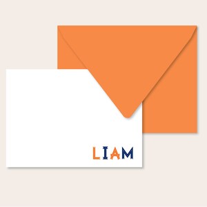 May include: A white card with the name "LIAM" printed in blue and orange letters. The card is sitting on top of an orange envelope.