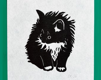 May include: A black and white linocut print on paper featuring a stylized, fluffy creature with pointed ears and a textured coat. The artwork displays a high-contrast silhouette of the animal sitting down, with the artist's initials LK and the year 26.